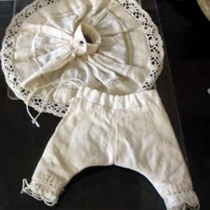 May include: A set of antique doll clothes, including a white cotton skirt with lace trim and a pair of white cotton pants with lace trim.