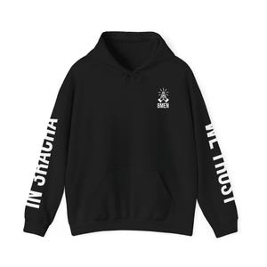 May include: Black hoodie with a front pocket and a drawstring hood. The left sleeve reads "IN GRACIA" in white block letters, and the right sleeve reads "WE MUST" in white block letters. The chest features a white graphic and the text "8MEN".