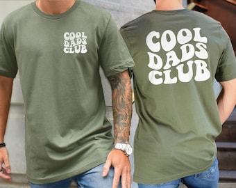 May include: Olive green t-shirt with the text "COOL DADS CLUB" in white, on both the front and back. The front features a smaller logo on the chest. The shirt is a casual, short-sleeved style.