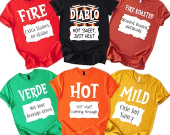 May include: A collection of six colorful t-shirts with text. The shirts are red, black, rust, green, orange, and yellow. The text on the shirts includes "FIRE", "DIABLO", "FIRE ROASTED", "VERDE", "HOT", and "MILD".