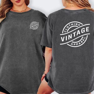 a woman wearing a gray t-shirt with the text "CLOTHING VINTAGE APPAREL" printed on the back.