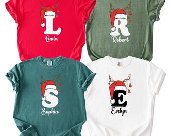 May include: Four short-sleeved t-shirts in red, green, teal, and white. Each shirt features a large initial, a Santa hat, and reindeer antlers. The names "Linda", "Robert", "Sophia", and "Evelyn" are printed below the initials.