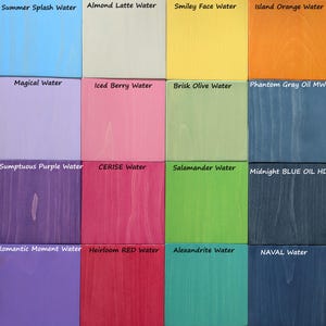 May include: A grid of sixteen wooden squares, each painted a different color. The colors include light blue, beige, yellow, orange, lavender, pink, green, and various shades of purple, red, and blue. Each square has a label with a color name, such as "Summer Splash Water."