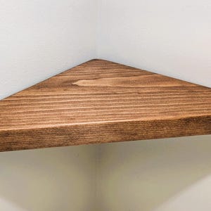Peut inclure: Une étagère triangulaire en bois avec une finition teintée brun foncé. L'étagère est en bois massif et a une surface lisse et polie.