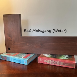 May include: A red mahogany wooden shelf with an L-shaped design. The shelf is supported by two books with colorful covers. The text "Red Mahogany (Water)" is visible on the wall behind the shelf.