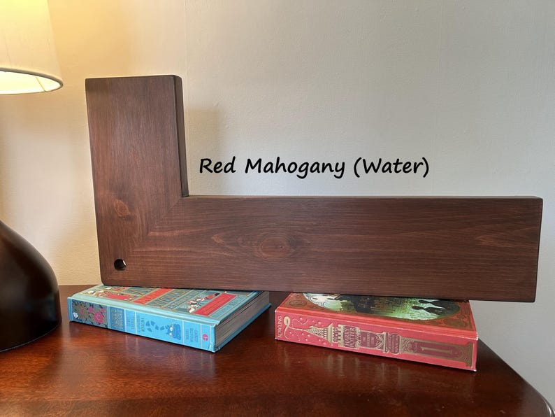 May include: A red mahogany wooden shelf with an L-shaped design. The shelf is supported by two books with colorful covers. The text "Red Mahogany (Water)" is visible on the wall behind the shelf.