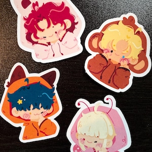 May include: Four colorful stickers featuring cartoon characters in animal-themed hoodies. The stickers include a pink bunny, a brown bear, an orange fox, and a pink butterfly. Each character has unique hair and facial features.