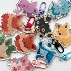May include: A collection of clear acrylic keychains featuring various colorful cartoon creatures with distinct designs. Each keychain includes a metal lobster clasp in matching colors like red, black, pink, blue, and purple, attached to the acrylic charms.