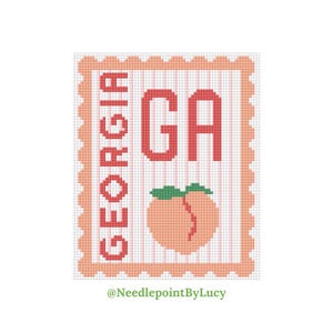 Puede incluir: Un diseño de punto de cruz rosa y blanco con un melocotón con una hoja verde y el texto "GEORGIA GA" en letras rojas. El diseño está enmarcado con un borde rosa festoneado.
