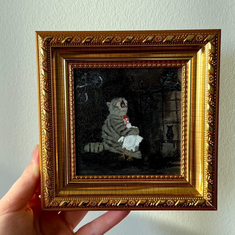 May include: A framed painting featuring a gray tabby cat holding a white chicken. The cat is in a dark room with a fireplace and a small black vase. The frame is gold with ornate detailing.