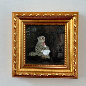 May include: A framed painting depicts a gray tabby cat holding a white chicken. The cat is seated with its mouth open, and the chicken is held in its paws. The painting is set in a dark room and framed in a gold ornate frame.