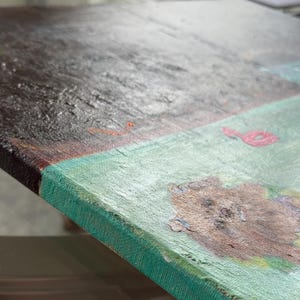 May include: Close-up of a textured painting on canvas. The artwork features a dark brown and gray section, a light green area, and a red abstract shape. The edges of the canvas are a darker green.