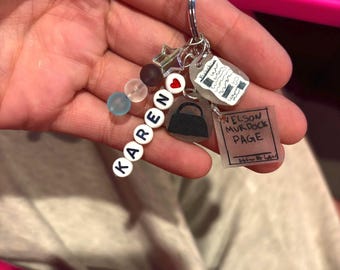 May include: A personalized keychain with the name "KAREN" spelled out in white letter beads. The keychain includes charms of a purse, a newspaper, a book with the text "NELSON MURDOCK PAGE", and other decorative beads and charms.