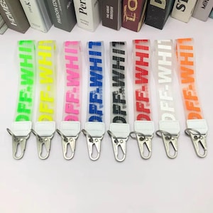 May include: A collection of clear, colorful wrist straps with the text "OFF-WHITE" in various colors, including green, yellow, pink, blue, black, red, and orange. Each strap has a silver clasp and a white leatherette patch.