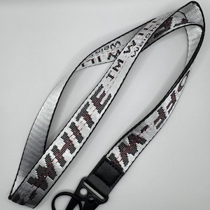 May include: A silver and black lanyard with the word "WEIGH" and other text in a repeating pattern. The lanyard has a black leather end piece and a black metal clasp.