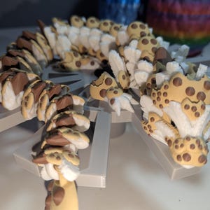 May include: A detailed, 3D-printed sculpture of a stylized, segmented creature with a tan and brown spotted pattern. The sculpture is mounted on a gray, geometric base, showcasing intricate details and textures. The creature's head is prominent, with a textured surface.