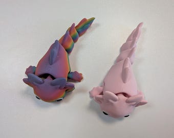 May include: Two articulated axolotl figures, one featuring a vibrant rainbow gradient pattern and the other in a solid light pink color. Both creatures have prominent external gills, dorsal fins, and segmented tails, showcasing a 3D printed texture.