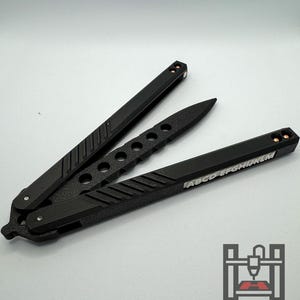 Può includere: Un coltello a farfalla nero con un'impugnatura testurizzata e un'iscrizione argentata che recita "ABCDEFGHIJKLM".