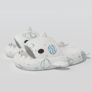 May include: A pair of white shark-shaped slides with blue planet and star graphics. The slides have black eye details and a textured, toothed mouth design. The overall theme is space and aquatic life.