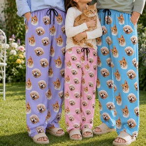 May include: Three pairs of lounge pants featuring an all-over print of dog and cat faces. The left pair is light purple, the center pair is light pink, and the right pair is light blue. Each pair has a black drawstring at the elastic waistband.