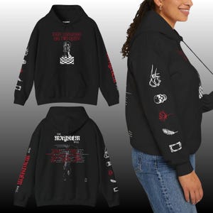 Może przedstawiać: Czarna bluza z kapturem z białą i czerwoną grafiką. Przód przedstawia napis "EVERY CHESSBOARD HAS TWO QUEENS" nad wzorem szachowym. Rękawy mają różne ilustracje. Tył bluzy z kapturem ma napis "THE MAYHEM BALL" i grafikę.