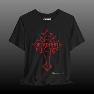 May include: Black t-shirt featuring a red graphic of a cross with the words "The Mayhem Ball" and "Tour 2025/2026". The word "Mayhem" is printed in white at the top of the shirt.