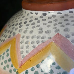 Op de afbeelding: Een keramische kom met een witte basis, versierd met een patroon van grijze stippen en kleurrijke geometrische ontwerpen. De kom heeft roze, gele en groene accenten en een bruine rand.
