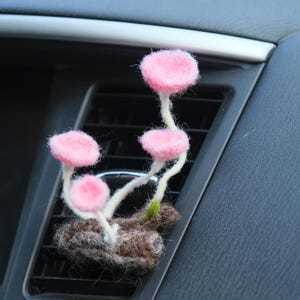 May include: A pink felt mushroom car air freshener with a brown felt base. The mushroom is attached to a white felt stem.