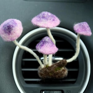 May include: A cluster of four purple and pink felt mushrooms attached to a brown felt base. The mushrooms are arranged in a car's air vent.