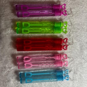 May include: Six pairs of bubble wands with heart-shaped charms. The wands are clear plastic tubes filled with bubble solution and have a heart-shaped wand attached. The charms are silver and have a heart shape.
