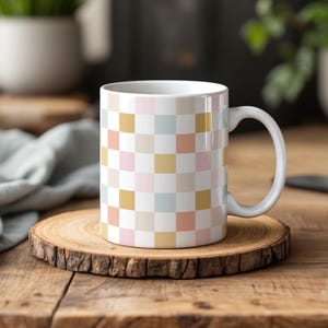 Puede incluir: Taza de cerámica blanca con un patrón a cuadros en rosa, azul claro y dorado. La taza tiene un asa blanca.