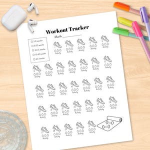 May include: A white Workout Tracker sheet with a month section, workout duration options, and spaces for daily activity tracking. Features illustrations of sneakers, water droplets, dumbbells, and a yoga mat. Colorful pens and wireless earbuds are also visible.