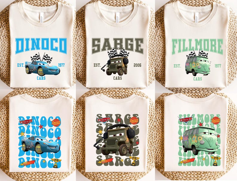 May include: Cream-colored t-shirts featuring cartoon car graphics and text. Designs include "DINOCO," "SARGE," and "FILLMORE," with additional text like "EST. 1977" and "CARS." The shirts are displayed on a woven surface.