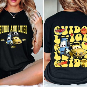May include: Black t-shirt featuring the text "GUIDO AND LUIGI" above a graphic of two cartoon cars. The front design includes "EST. 1977 CARS". The back of the shirt has a similar design with the text "Cars" and "Rusteze".