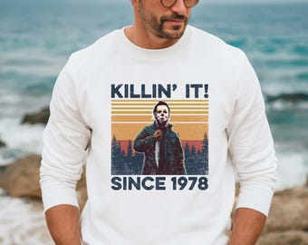 May include: White sweatshirt with a vintage-style graphic of a masked figure holding a knife. The graphic says "Killin' It! Since 1978".