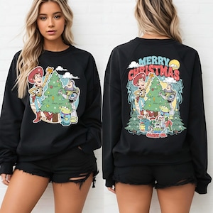 Puede incluir: Sudadera negra con un gr&aacute;fico navide&ntilde;o de dibujos animados. La parte delantera muestra a Woody y Buzz Lightyear con un &aacute;rbol de Navidad. La parte trasera de la sudadera tiene las palabras "Merry Christmas" y otros personajes.
