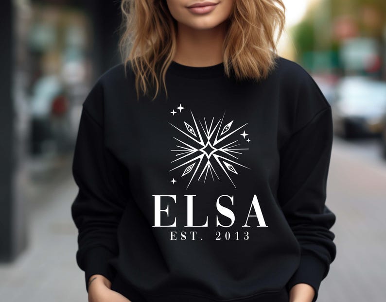 Puede incluir: Sudadera negra con un dise&ntilde;o de estrella blanca y el texto "ELSA EST. 2013" impreso en la parte delantera.