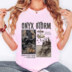 Puede incluir: Camiseta rosa con un estampado gr&aacute;fico en blanco y negro que representa un drag&oacute;n, un castillo y un libro. El texto "ONYX STORM" est&aacute; impreso en negro en la parte superior del gr&aacute;fico. El texto "I WILL NOT DIE TO DAY I WILL SAVE HIM" est&aacute; impreso en negro debajo del gr&aacute;fico. El texto "BASGIATH WAR + COLLEGE" est&aacute; impreso en negro en la parte inferior del gr&aacute;fico.