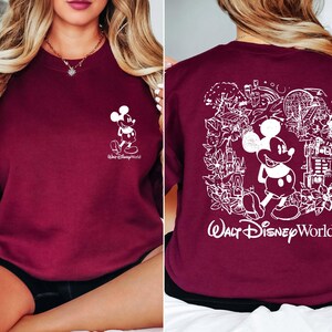 May include: Burgundy sweatshirt with a white Mickey Mouse graphic on the front and a white Mickey Mouse graphic with a scene of Walt Disney World on the back. The text "Walt Disney World" is printed below the graphic.