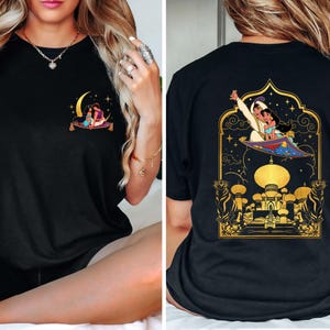 May include: Black t-shirt with a graphic print of Aladdin and Jasmine flying on a magic carpet over a golden palace. The graphic is surrounded by stars and a crescent moon.