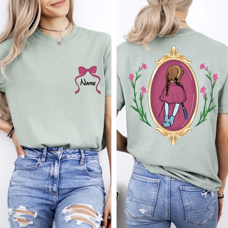 May include: Sage green t-shirt with a pink bow and the word "Name" printed on the front. The back features an illustration of a girl in a frame with pink flowers and green leaves.