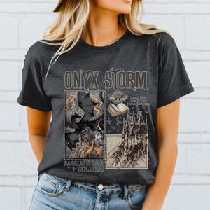 Puede incluir: Una camiseta gris oscuro con un estampado gr&aacute;fico de un murci&eacute;lago negro, un libro y un castillo. El texto "ONYX STORM" est&aacute; impreso en blanco sobre el gr&aacute;fico. El texto "BASGCLATH WAR COLLEGE" est&aacute; impreso debajo del gr&aacute;fico.