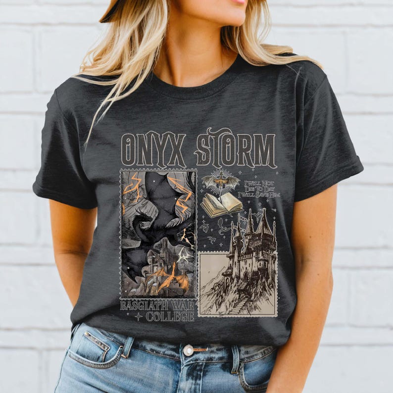 Puede incluir: Una camiseta gris oscuro con un estampado gr&aacute;fico de un murci&eacute;lago negro, un libro y un castillo. El texto "ONYX STORM" est&aacute; impreso en blanco sobre el gr&aacute;fico. El texto "BASGCLATH WAR COLLEGE" est&aacute; impreso debajo del gr&aacute;fico.