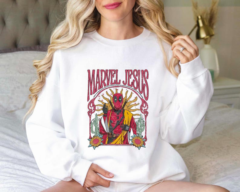 May include: White sweatshirt with a vintage-style graphic of Deadpool in a red and black suit with the text "Marvel Jesus" above him.