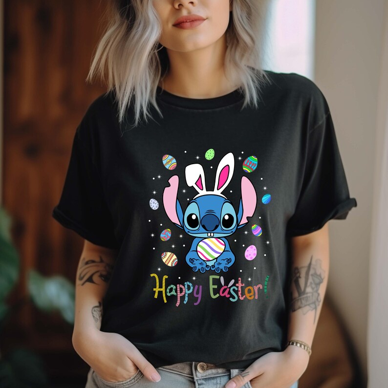 May include: A black t-shirt with a blue Stitch character wearing bunny ears and holding a colorful Easter egg. The text "Happy Easter" is printed below the character. The character is surrounded by colorful Easter eggs.