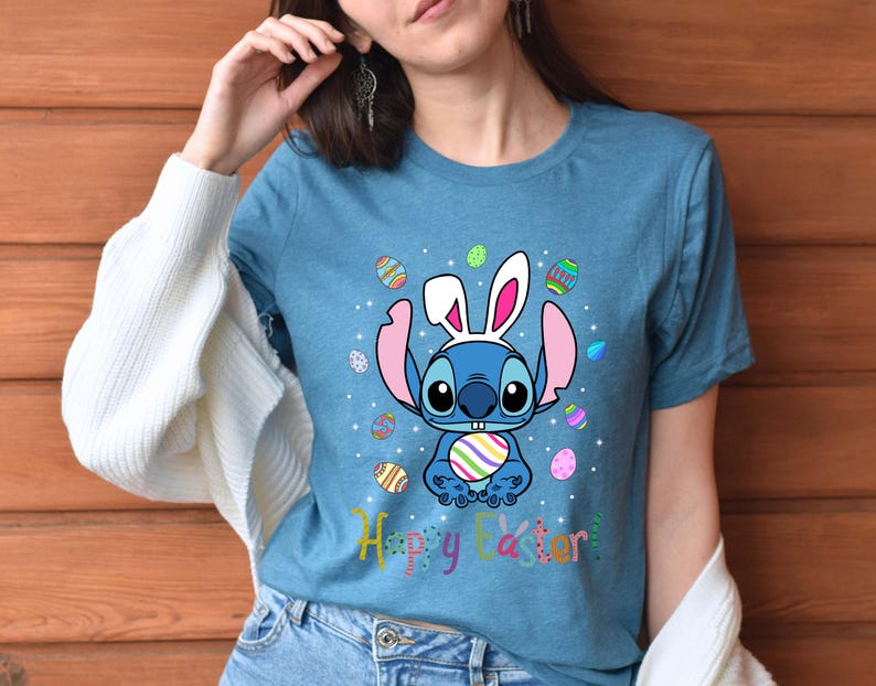 May include: A blue t-shirt with a cartoon Stitch wearing bunny ears and holding an Easter egg. The shirt has a colorful Easter egg pattern and the text "Happy Easter!"
