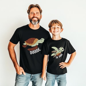 May include: A black t-shirt with a cartoon sea turtle and the text "DUUUDE". A smaller black t-shirt with a cartoon sea turtle and the text "Lil DUDE".
