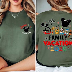 May include: An olive green sweatshirt with Disney graphics. The front has "Disney 2025" and a Mickey Mouse head, with space for a custom name. The back shows "Disney Family Vacation 2025" with Disney characters.