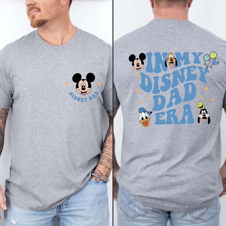 Puede incluir: Una camiseta gris con un gr&aacute;fico de Mickey Mouse en la parte delantera y el texto "In My Disney Dad Era" con gr&aacute;ficos de Mickey Mouse, Donald Duck y Goofy en la parte posterior.