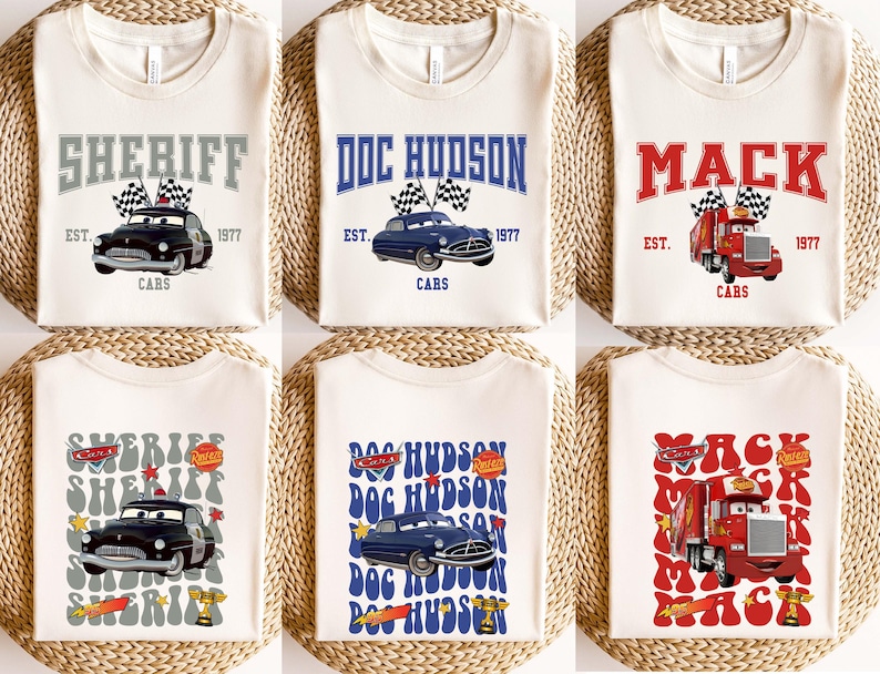 May include: Cream-colored t-shirts featuring cartoon car designs. The shirts display the names "SHERIFF", "DOC HUDSON", and "MACK" in various fonts, along with the text "EST. 1977" and "CARS". Each design includes a car graphic.